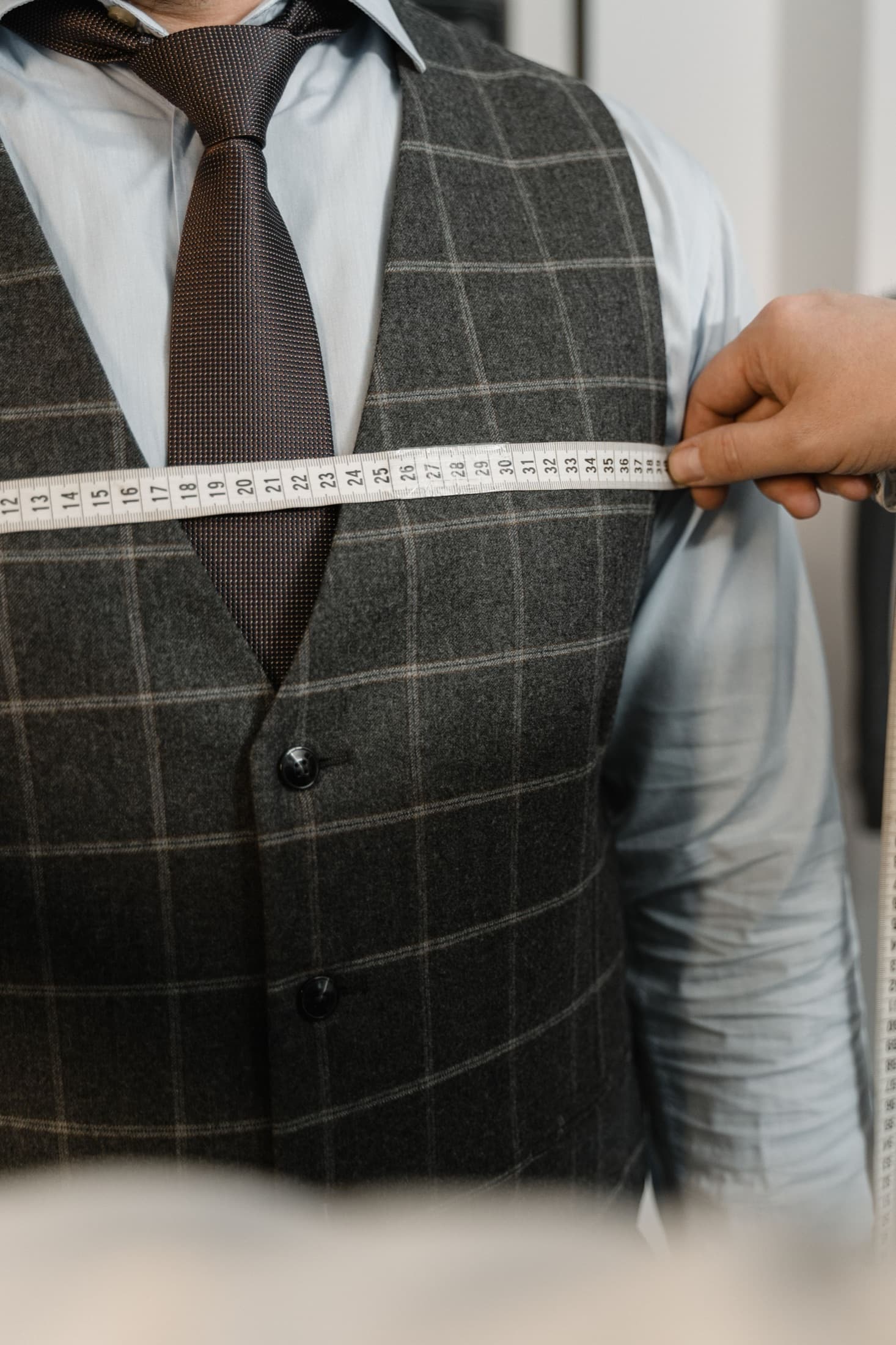 Tailor measuring a waistcoat across the chest with a tape measure